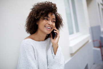 Wall Mural - close up happy smiling african american young woman talking with mobile phone outside by white wall