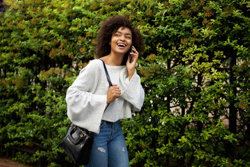 Wall Mural - happy african american woman talking with cellphone by trees