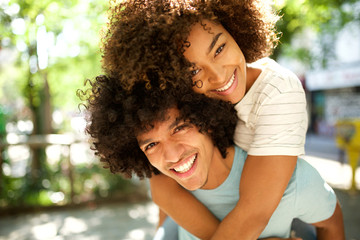 Wall Mural - happy guy giving smiling girl piggyback outdoors