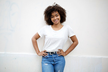 Wall Mural - beautiful african american girl with curly hair posing by white background with hands on hips