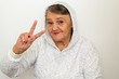 An older hipster woman. Nice shot of a gangster grandma. The old woman dressed in the style of hip-hop, her mood is elated.The old woman shows a peace sign.