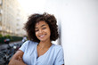 © mimagephotos - smiling young african american woman leaning against wall outside
