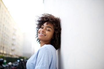 Wall Mural - Close up beautiful smiling young african american woman leaning against wall outside