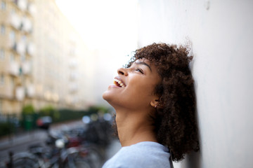 Wall Mural - side portrait of beautiful smiling young african american woman leaning against wall outside