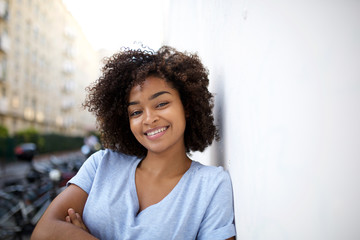 Wall Mural - smiling young african american woman leaning against wall outside