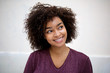 © mimagephotos - happy young african american woman with curly hair by white wall glancing