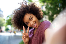 happy african american woman taking selfie with peace hand sign outside