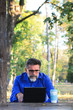 © Nenad - Handsome bearded Middle age businessman Casual dressed using a laptop and taking notes while sitting in cafe in the park outdoor. Portrait of a smiling Middle age man sitting outside