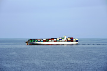 Large cargo container ship, fully loaded with colorful containers, sailing through the calm ocean near Japanese island Hokkaido. 