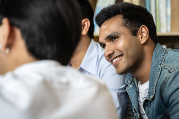 Indian businessman sitting in office and speaking on the phone with colleagues meeting in the background