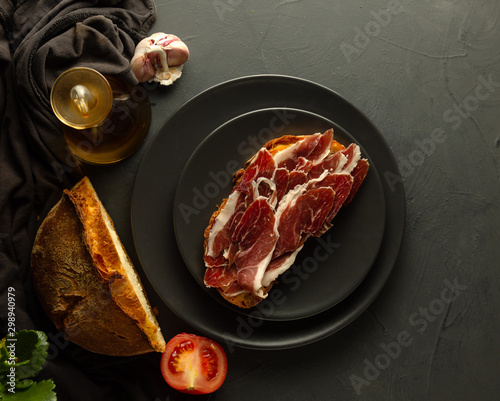 Fotografía Toasted bread with Iberian ham on black plates and rustic background - zenith vi
