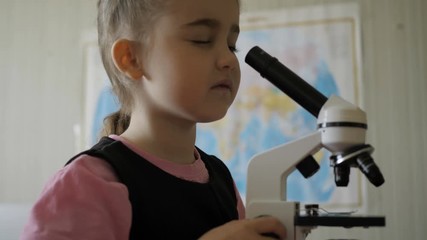 little girl in science lab study samples under microscope. schoolgirl looking through microscope in 