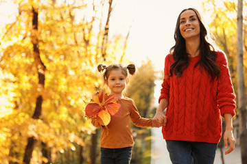 Wall Mural - Happy woman with daughter walking in sunny autumn park