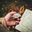© OlegKovalevich - A man holds a compass and a paper map in his hand and is guided by the area, autumn forest, walk,hiking