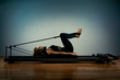 © Georgii - Young girl doing pilates exercises with a reformer bed. Beautiful slim fitness trainer on a reformer gray background, low key, art light, copy space advertising banner