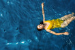 © Alexander - young woman in a one-piece yellow swimsuit floats on the surface of the water.