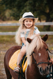 Adorable little girl riding a pony at summer