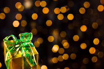 Wall Mural - Closeup present gift box wrapped in gold paper with green bow. Festive decorative garland with yellow light bulbs, lanterns are shining on background. New year, christmas mood. Greeting card.