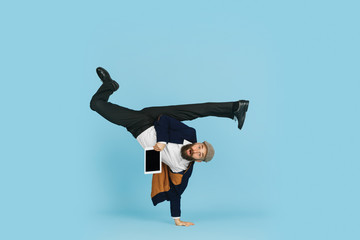 Wall Mural - Young caucasian businessman having fun dancing break dance on blue studio background. Management, flexible, freedom, professional occupation, alternative way of modern working. Loves his job