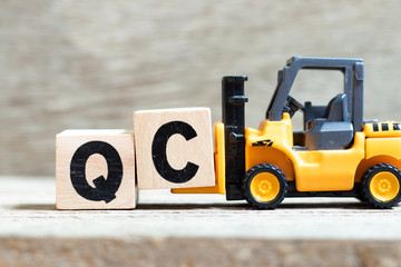 Wall Mural - Toy forklift hold letter block c to complete word QC (Abbreviation of Quality Control) on wood background