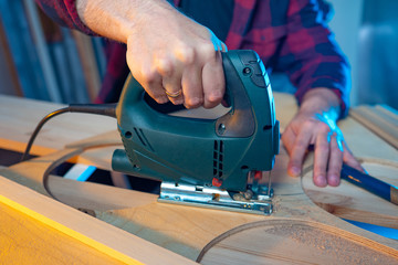 Poster - Carpenter's hands with electric jigsaw close-up. Work in a carpentry workshop. A man cuts plywood with an electric jigsaw. Electric tool for woodworking. Sawing wood fragments of the future product.