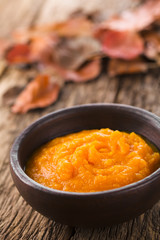 Wall Mural - Fresh homemade pumpkin puree in bowl, colorful autumn leaves in the back (Selective Focus, Focus one third into the dish)