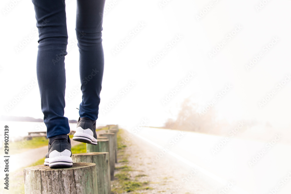 A woman walking on stump carefully next to the road. Concept of living life with confidence and take care every steps of moving forward to make sure life safe. Free copied space for text on right. - obrazy, fototapety, plakaty 