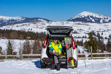 man sitting in car trunk changing for snowboard