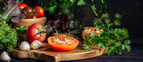 Fototapeta Natura - Fresh tomatoes and parsley, dill, garlic on a dark background in a rustic kitchen and wooden utensils still life with copy space