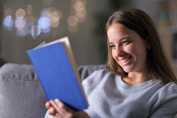 Wall Mural -  Happy woman reading a paper book on a couch in the night