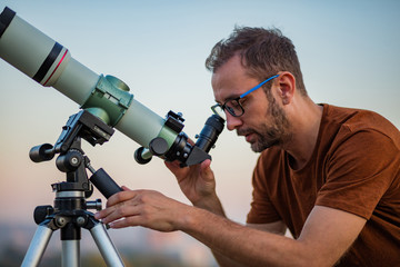 Wall Mural - astronomer with a telescope watching at the stars and moon with blurred city background.