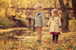 © Natalia - brother and sister holding hands standing at the pond in the park in fall season