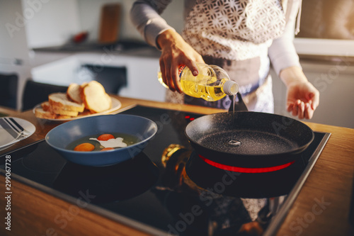 Fotomural Cropped picture of woman in apron pouring oil in frying pan while standing next to stove