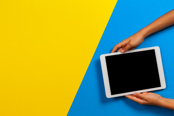 Wall Mural - Kid hand with tablet computer on yellow and light blue background