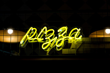 Glowing Neon yellow sign PIZZA and blurred lights on black background