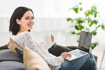 Wall Mural - cheerful girl with cup of tea using laptop at cozy home