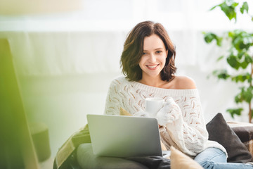 Wall Mural - attractive smiling girl with cup coffee of using laptop at cozy home