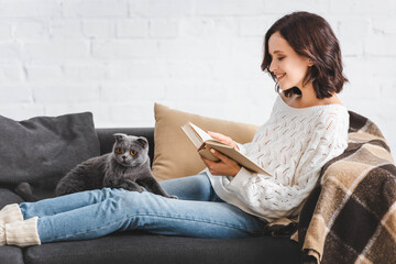 Wall Mural - happy girl reading book with scottish fold cat on sofa