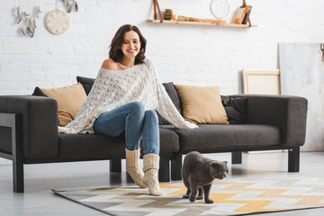 Wall Mural - beautiful happy woman sitting on sofa with scottish fold cat on floor