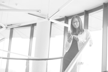 Wall Mural - Black and white photo of businesswoman using on smartphone while standing at office