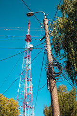 Lamp pole  lot of electric wires hangs from above the TV tower at blue sky background, Yoshkar-Ola city