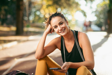 Young fitness woman in park. Athletic woman sitting on  running track and using phone.