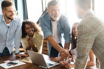 Canvas Print - Welcome to our team! Business men in smart casual wear shaking hands while working in the creative office.