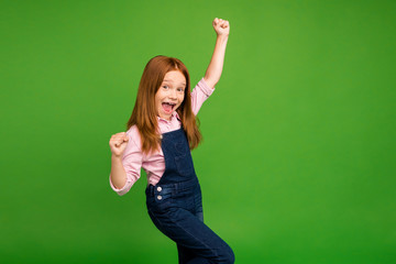 Poster - Profile photo of little ginger schoolchild celebrating winning classmates team in sportive competitions raise fists wear denim overall pink shirt isolated green background