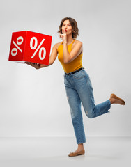 Sticker - shopping, consumerism and people concept - happy smiling young woman in mustard yellow top and jeans with sale sign making hush gesture over grey background