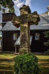 Wall Mural - Stone cross on the background of the wooden Church of St. Lawrence (Wawrzyniec) in Grojec, Poland. 