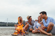 © BalanceFormCreative - Group of friends sitting by the camp fire at the beach.they singing and play guitar.Autumn season.