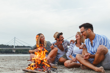 Group of friends sitting by the camp fire at the beach.they singing and play guitar.Autumn season.