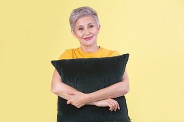 stylish beautiful aged woman with a pillow in hands on a yellow background