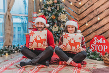 Classic New Year Tree Decoration, Boy And Girl In Santa Hats And Pillows With Deer Print In Their Hands.